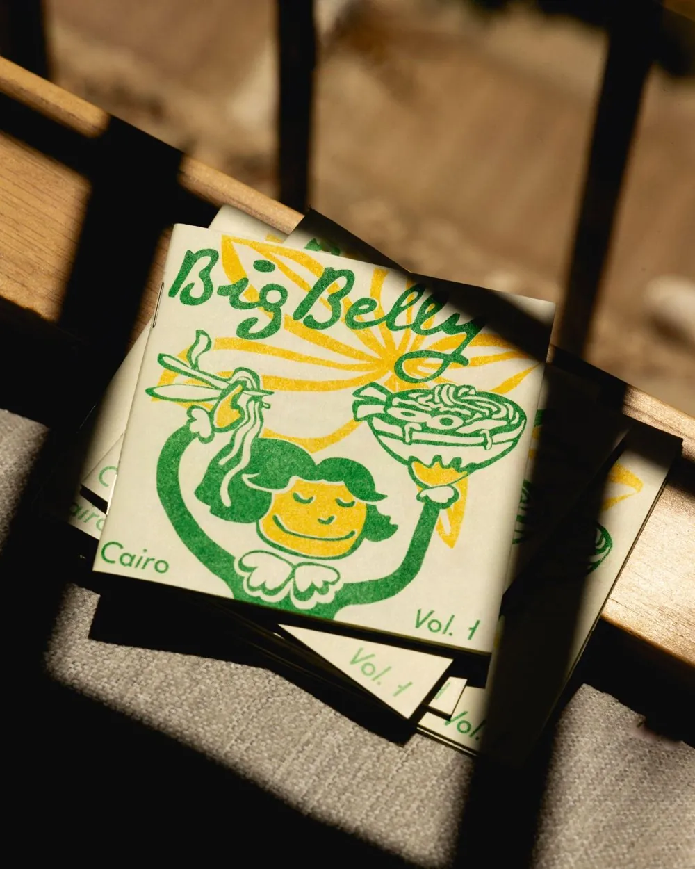 Big Belly Vol. 1 Cairo zines stacked on a chair in afternoon light